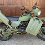 Green military motorbike parked in front of a wooden garage door
