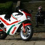 Motorbike rider sat on steps next to a parked up classic motorbike