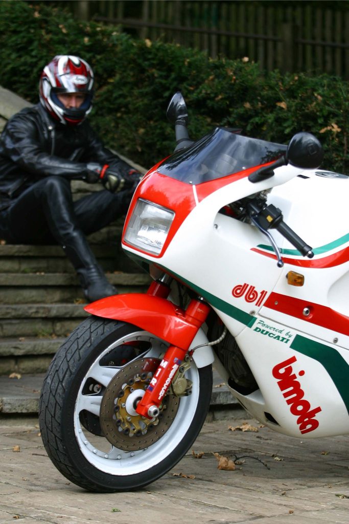 Motorbike rider sat on steps next to a parked up classic motorbike