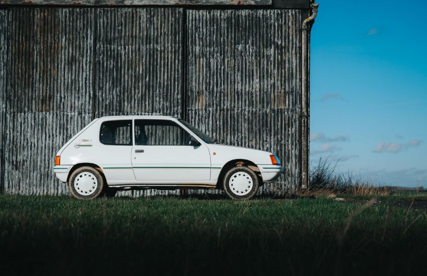 Side view of a white Peugeot 205 parked in front of a barn