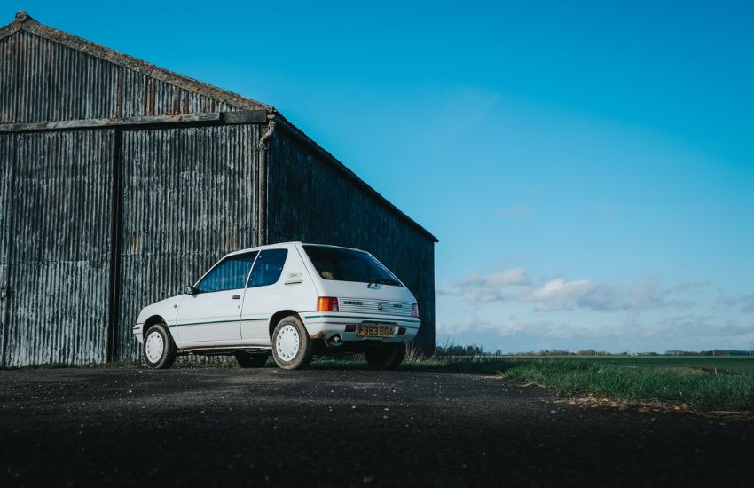 Rear view of a white Peugeot 205 parked in front of a barn