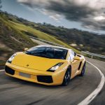 Yellow Lamborghini Gallardo V10 driving uphill around a bend in the road