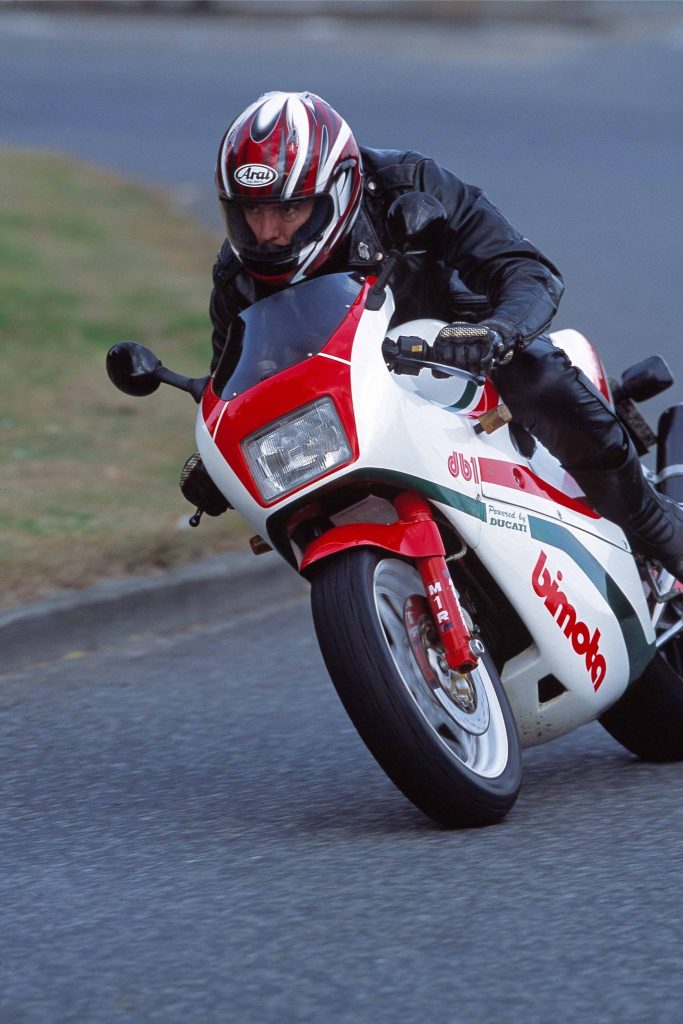 Man riding a white, red and green motorbike along a road
