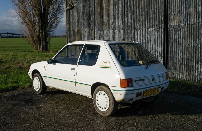 Rear view of a while Peugeot 205 parked in front of a barn