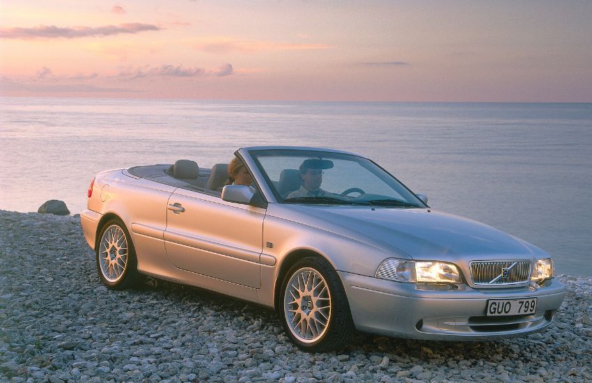 Two people sat in a silver convertible car parked on a beach