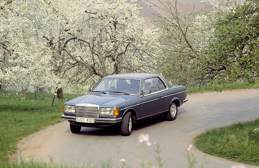 Mercedes W123 classic car driving around a bend in the road
