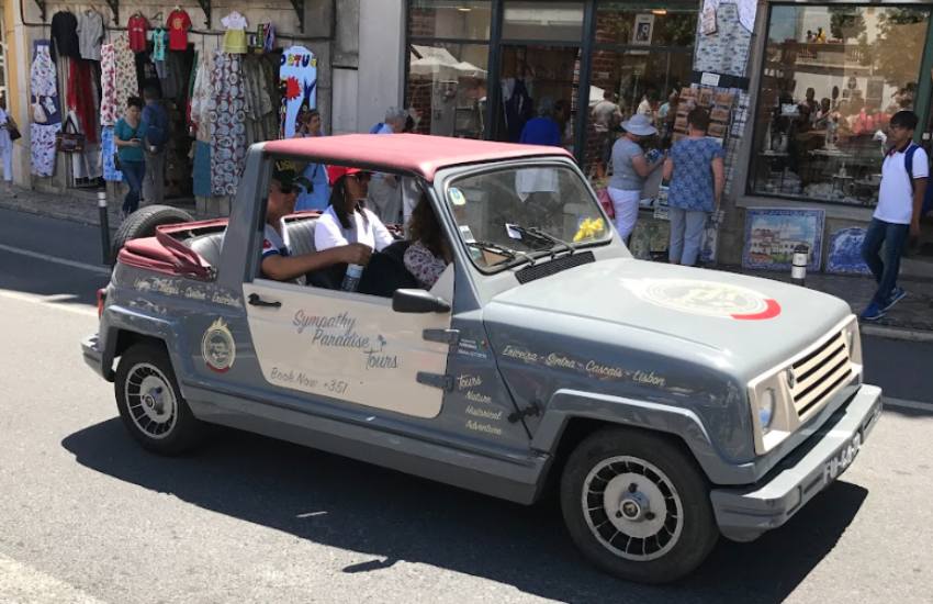 Grey convertible classic car with a red roof being driven through a busy street