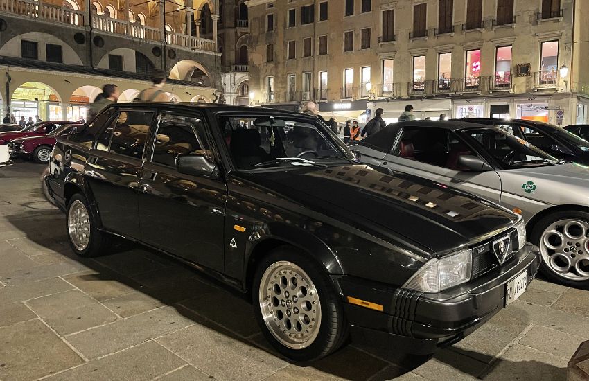Black Alfa Romeo 75 parked on a busy street at night time