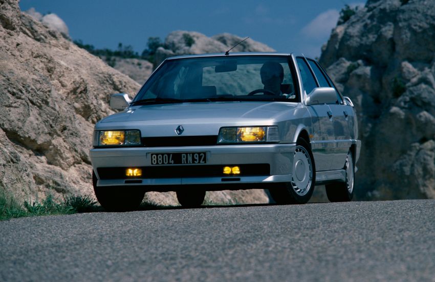 Silver Renault 21 with illuminated headlights being driven along a road