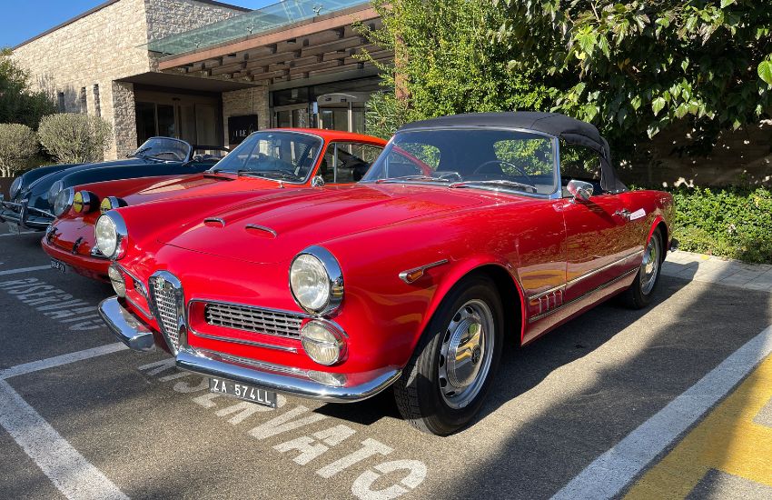 Red Alfa Romeo 2000 Spider reverse parked in front of bushes