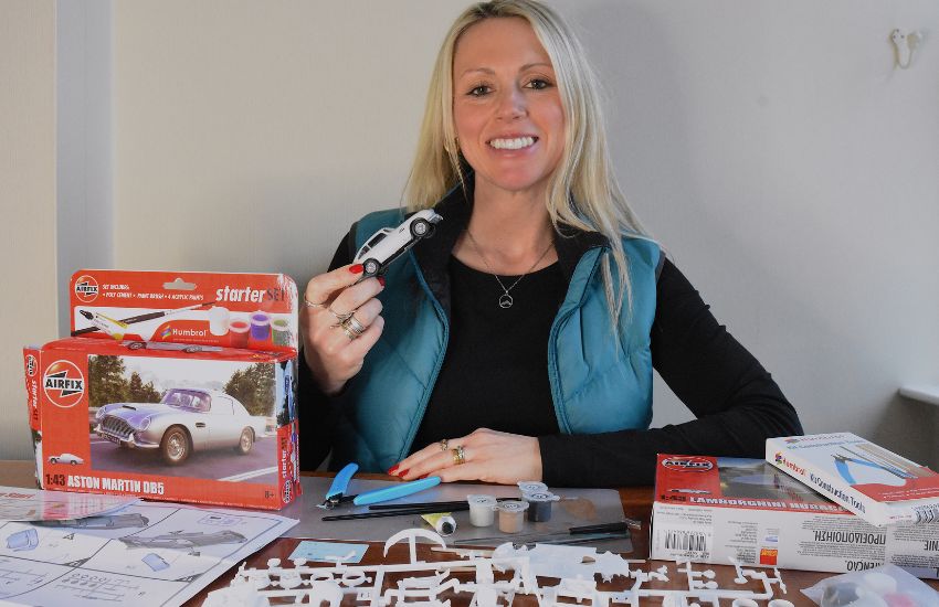 Woman sat down holding up Airfix model car smiling