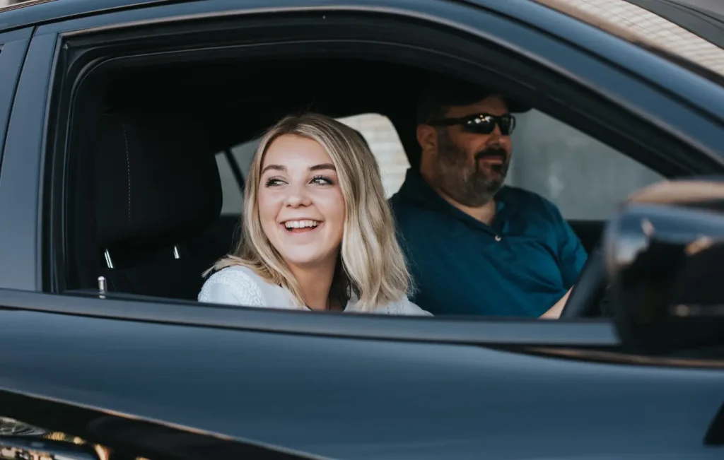 Young driver driving a classic car with a passenger beside her
