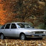 Woman stood next to a silver classic car parked in the woods