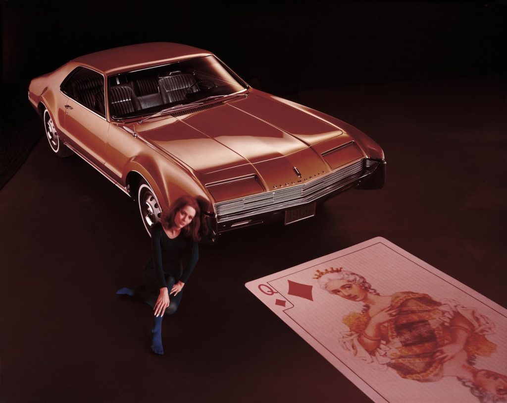 Lady sitting next to red Oldmobile Toronado