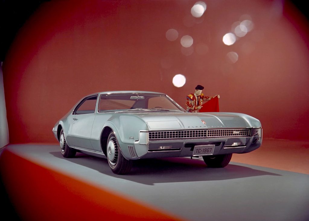 Front of grey Oldmobile Toronado on red background