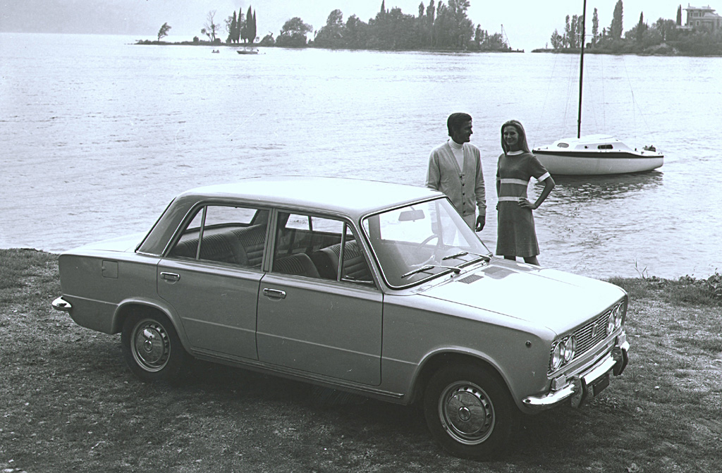 Two people stood next to a classic car in front of a lake
