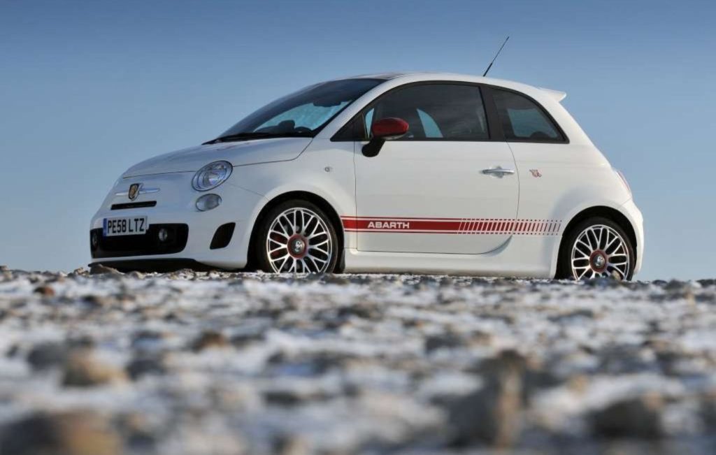 Side view of a white and red car parked on the side of a hill on a sunny day
