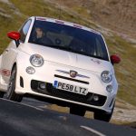 Man driving a white and red car along a hill side road