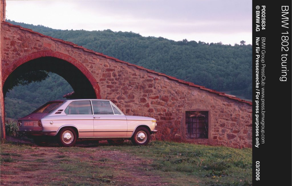 Silver classic car parked next to a stone building on a grassy hill