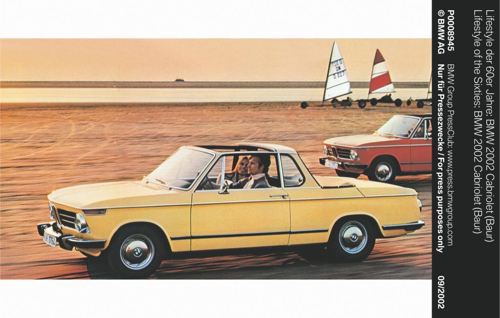 Man and woman driving in a yellow convertible classic car along a sandy beach