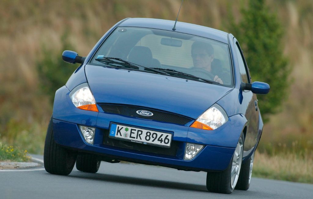 Man driving a metallic blue Ford Ka car along a road