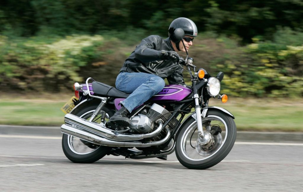 Man riding Candy Purple Kawasaki KH400 classic motorcycle along the road at speed