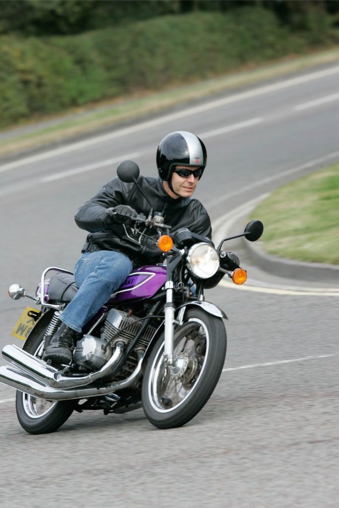 Front view of a man riding a classic motorbike around a bend in the road