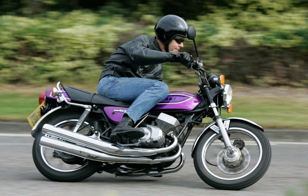 Man riding Candy Purple Kawasaki KH400 classic motorcycle along the road at speed