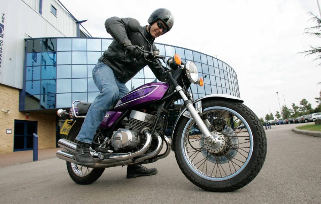 Rider sat on top of a purple classic motorbike in front of a glass building