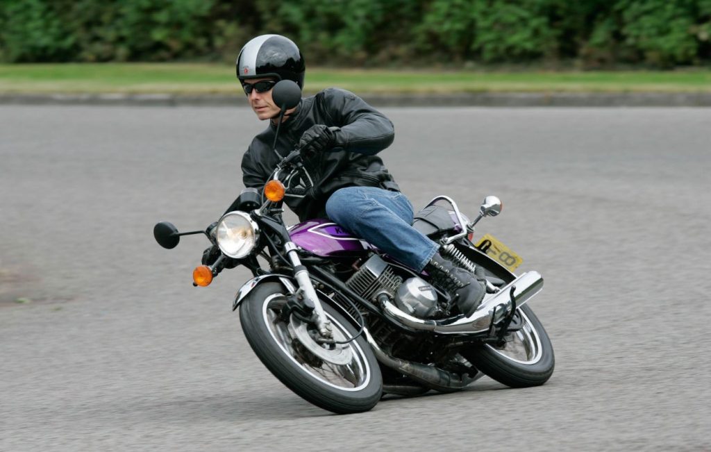 Man riding Candy Purple Kawasaki KH400 classic motorcycle along the road at speed