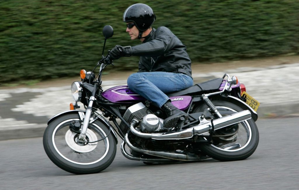Man riding Candy Purple Kawasaki KH400 classic motorcycle along the road at speed