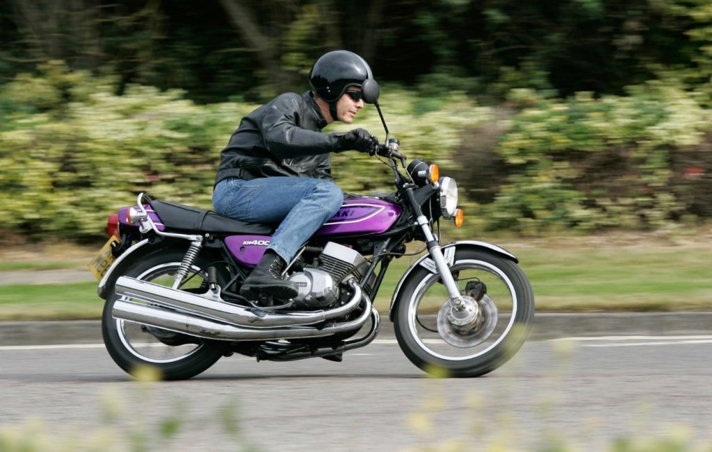 Man riding Candy Purple Kawasaki KH400 classic motorcycle along the road at speed