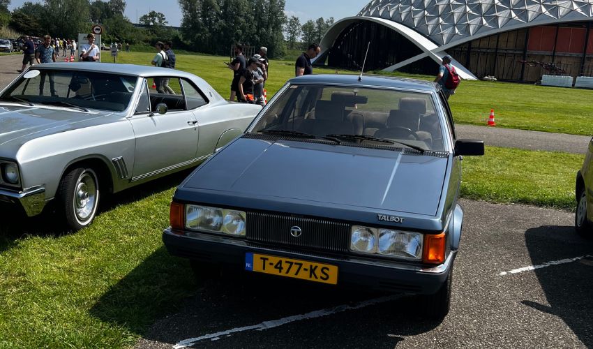 Two cars parked in front of a building at a car show