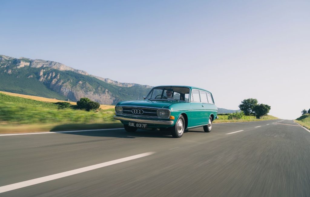 Man driving a turquoise Audi 80 estate along a country road