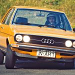 Man driving a yellow Audi 80 along a country road