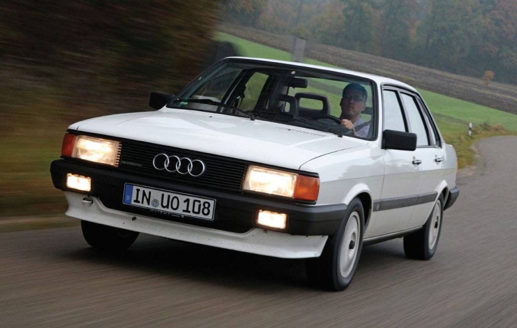 Man driving a white Audi 80 Quattro along a country road