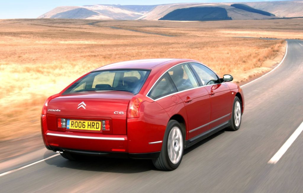 Rear view of a metallic red Citroen C6 driving along a road through moorland