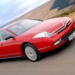 Red Citroen C6 being driven along a road in front of hills