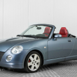 Parked metallic blue convertible Daihatsu Copen with the roof down