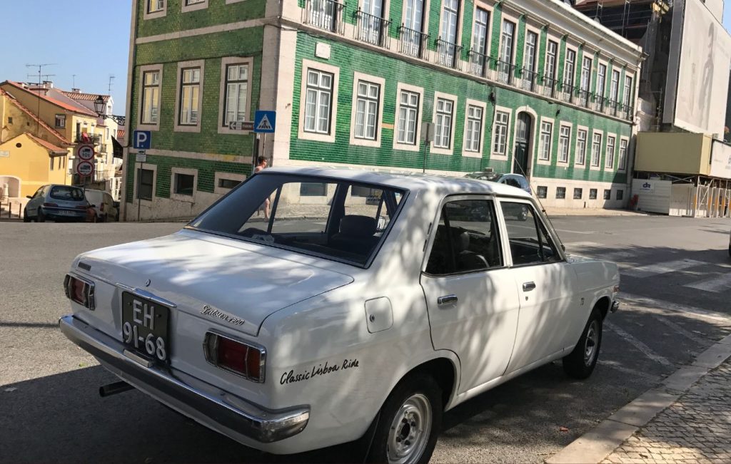A classic white Datsun 1200 sedan parked on a city street in Portugal