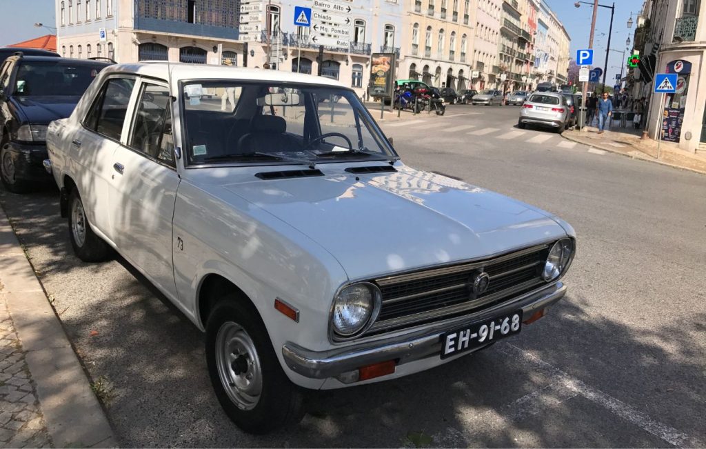 A classic white Datsun 1200 sedan parked on a city street in Portugal