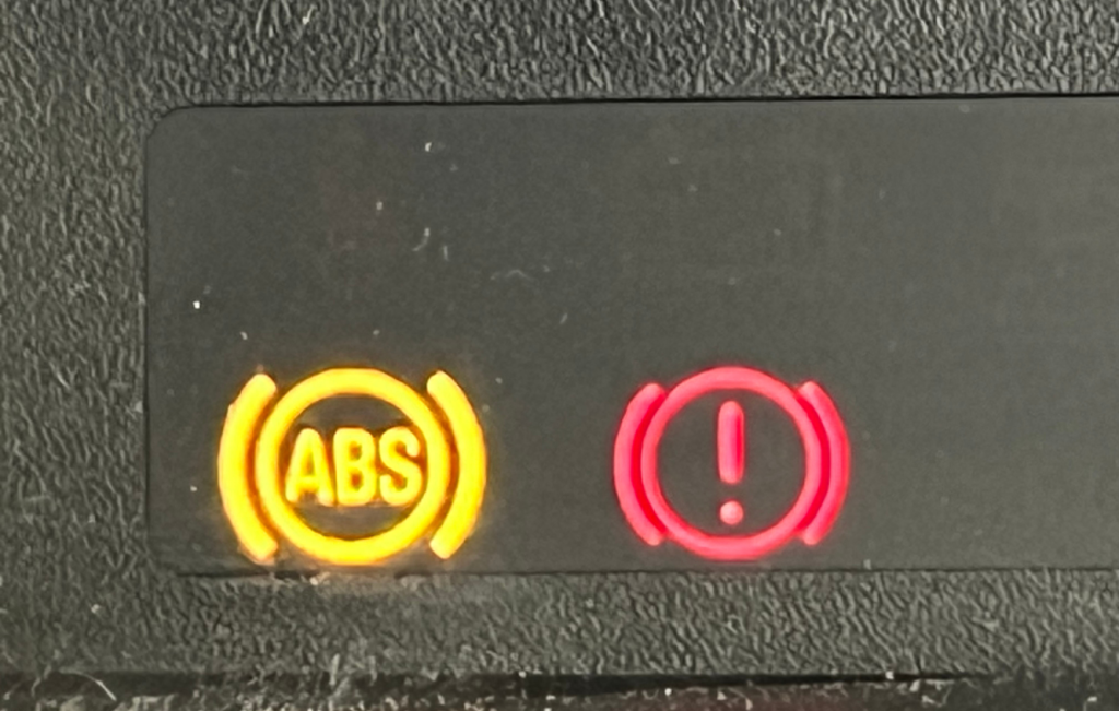 Red brake warning light and a yellow ABS fault message on the instrument cluster of a car