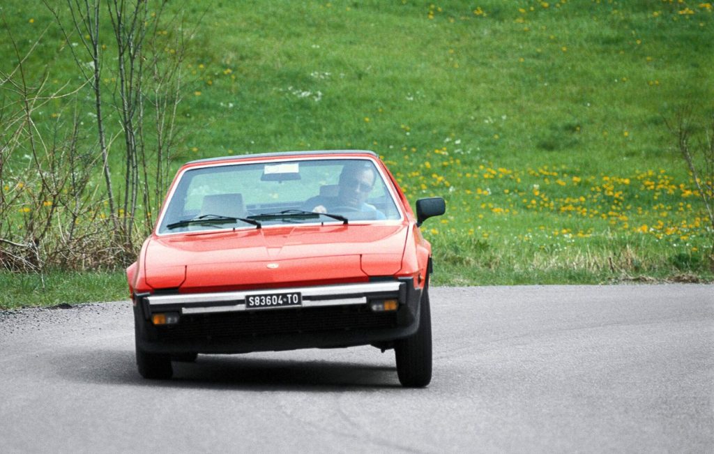 Man driving a red Fiat X1_9 around a corner in the road