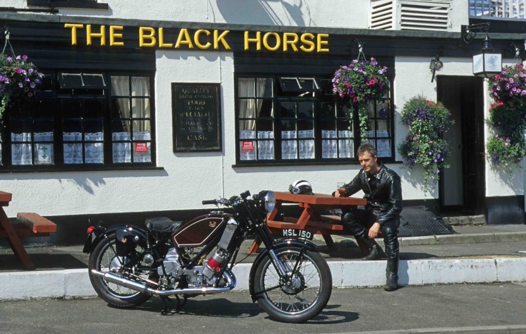 Man sat next to a Scott Flying Squirrel classic motorbike parked up in front of a pub