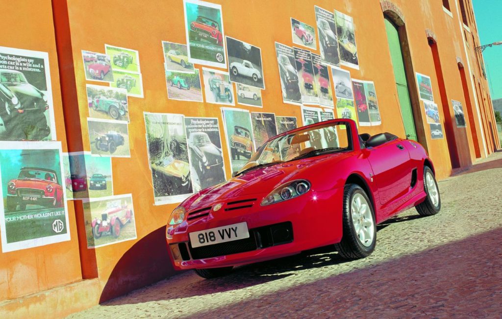 Red MG TF classic car parked in front of an orange building