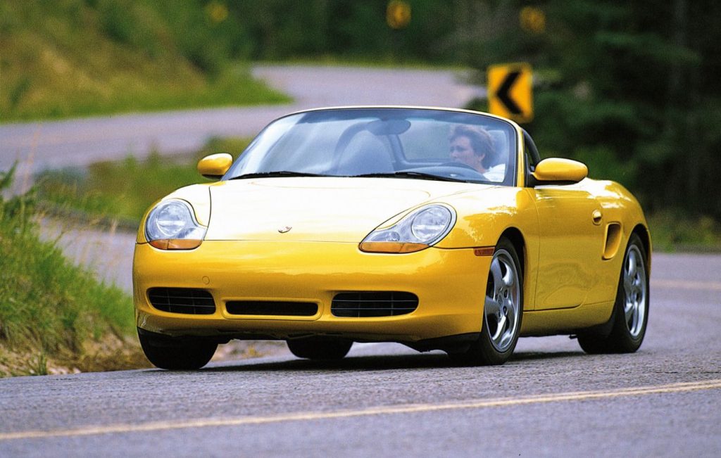 Woman driving a yellow Porsche Boxster 928 along winding country road