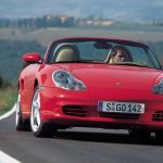 Man driving a red Porsche Boxster 986 along country road