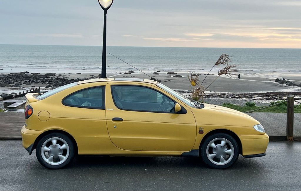 Side view of a yellow Renault Megane parked on a beachfront