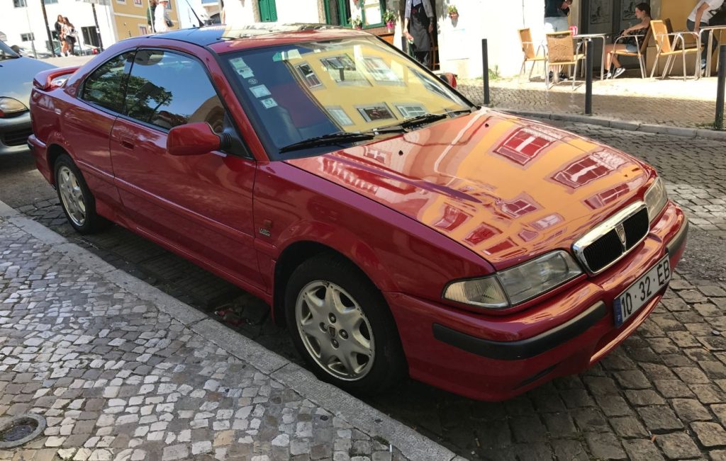 A red Rover 200 Coupé parked on a cobbled street
