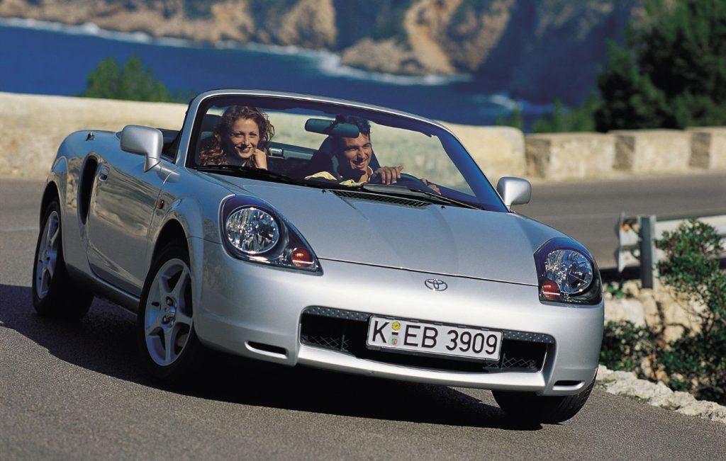 Man and woman in a silver Toyota MR2 MK3 driving along a road